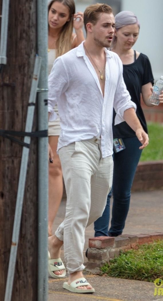 a man in white shirt and tan pants walking down the street with other people behind him