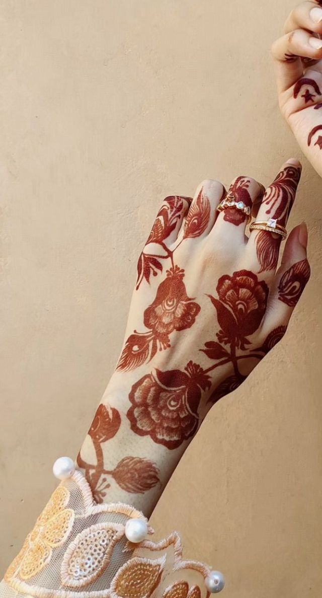 two hands with henna designs on them and one holding an object in the other hand