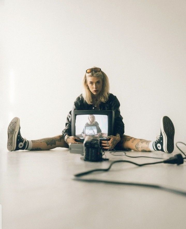 a woman sitting on the floor with her legs crossed and holding a camera in front of her