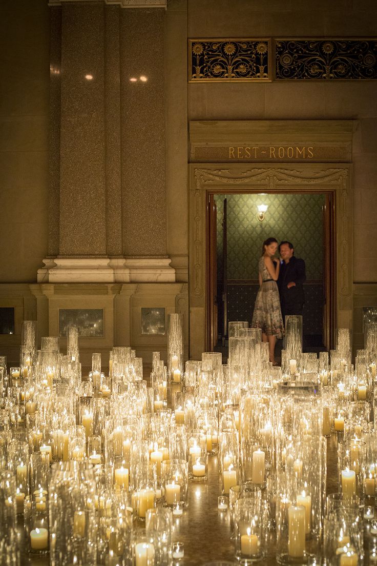 a man and woman standing in front of a large amount of candles