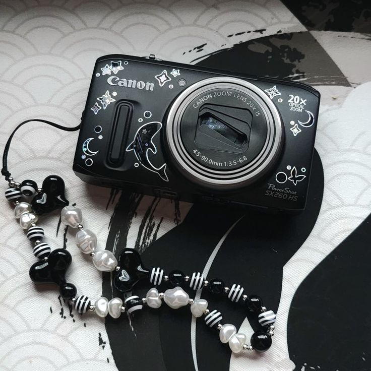 a black and white camera sitting on top of a bed next to a beaded necklace