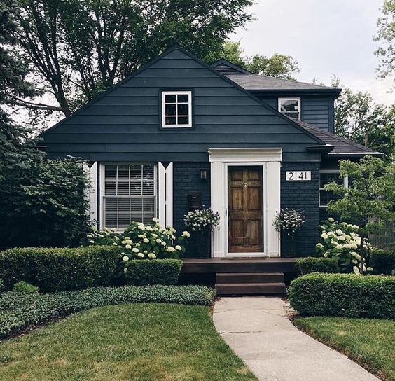 a black house with white trim and flowers on the front door is surrounded by greenery