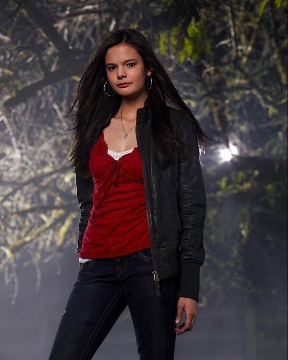 a beautiful young woman standing in front of a tree