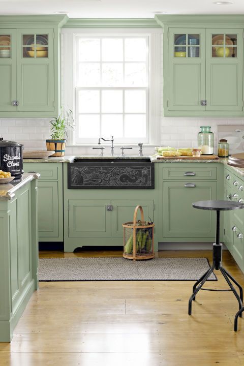 a kitchen with green cabinets and white walls, an island in the middle has a basket on it