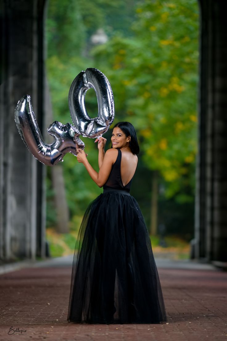 a woman in a black dress is holding some silver balloons that spell out the word love