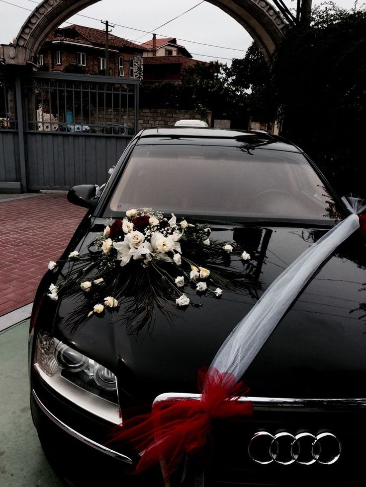 a black car with flowers on the hood and ribbon tied to it's front