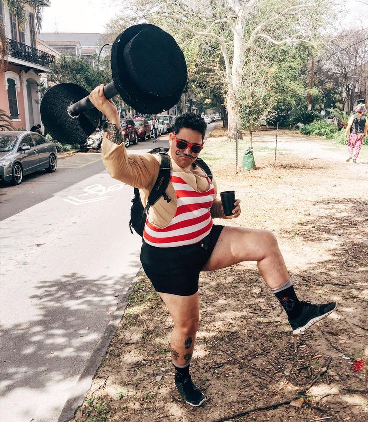 a man in shorts and striped shirt holding a pan on his head while posing for the camera