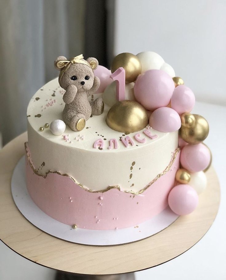 a pink and gold birthday cake with a teddy bear on top that says 1 in the middle