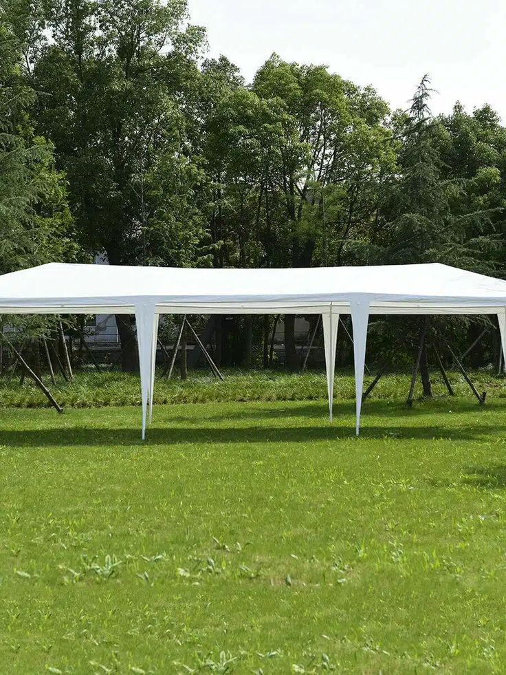 a large white tent set up in the middle of a field with trees behind it