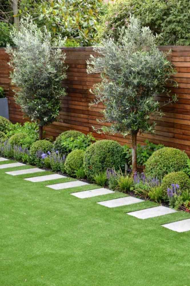 an outdoor garden with grass, trees and stepping stones in the center is lined by wooden fence