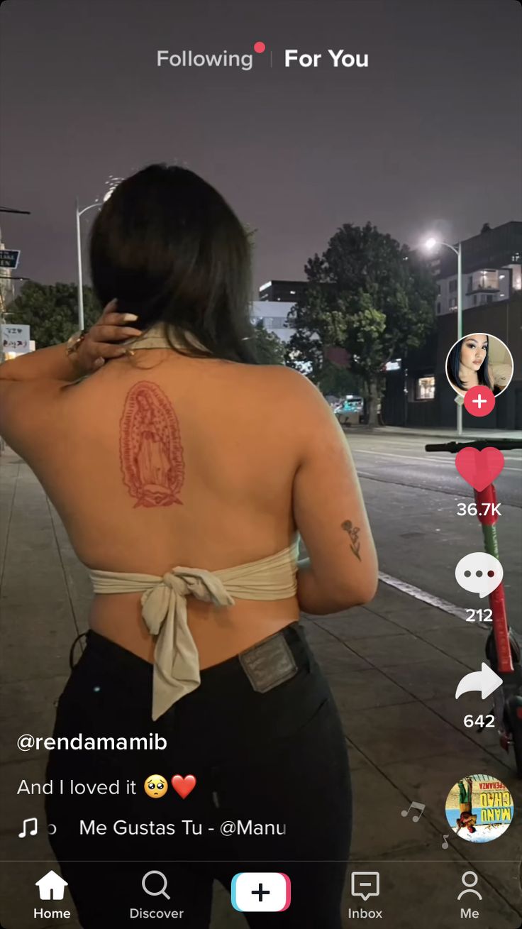 a woman with tattoos on her back walking down the street while holding a cell phone to her ear