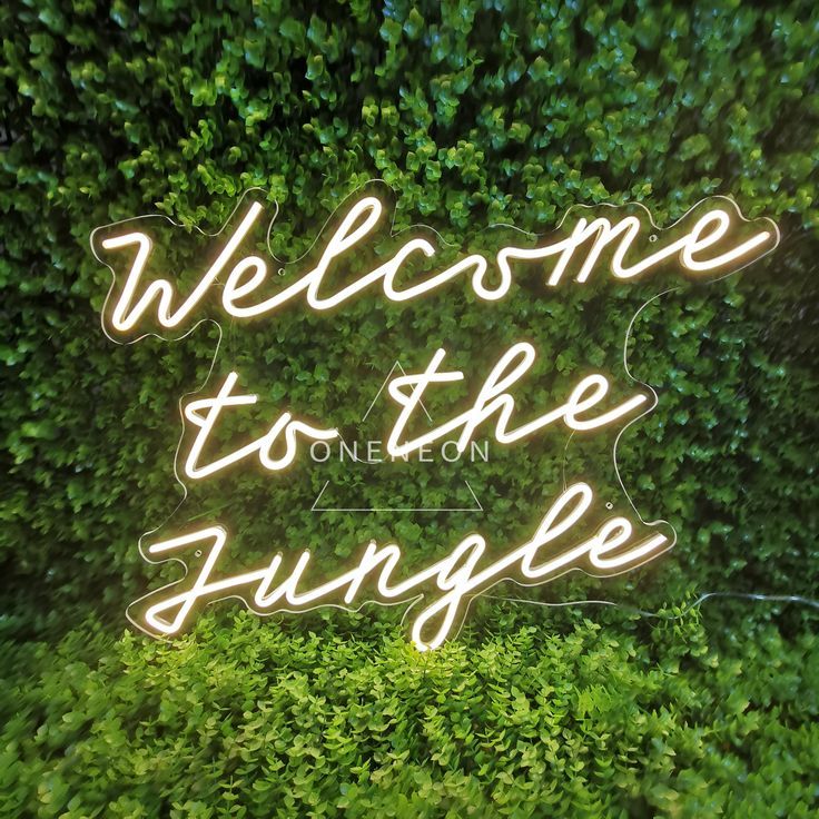 a neon sign that reads welcome to the jungle on top of a green plant covered wall