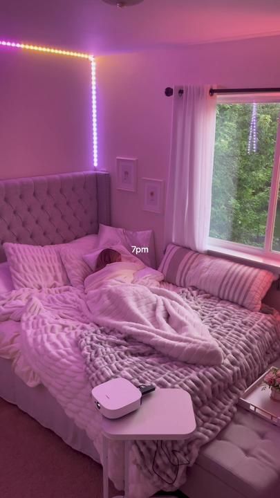 an unmade bed in a bedroom with pink lights on the windowsill and curtains