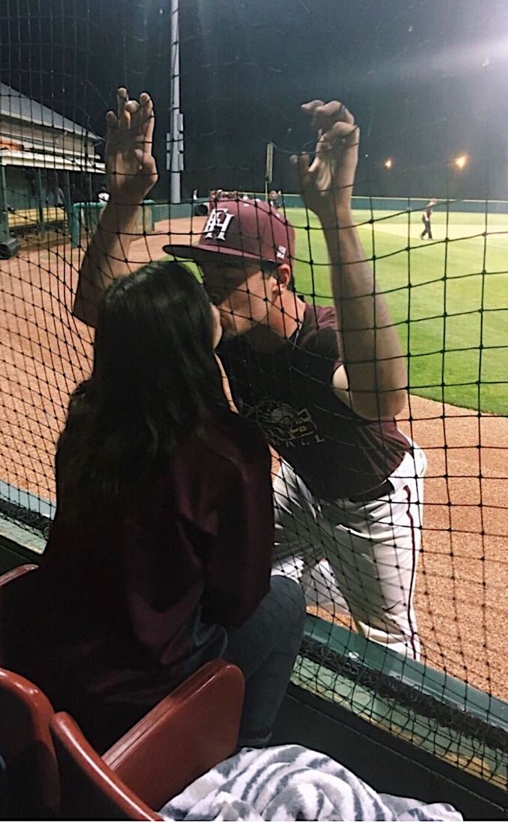 a person sitting in a chair at a baseball game holding up their hands to catch the ball