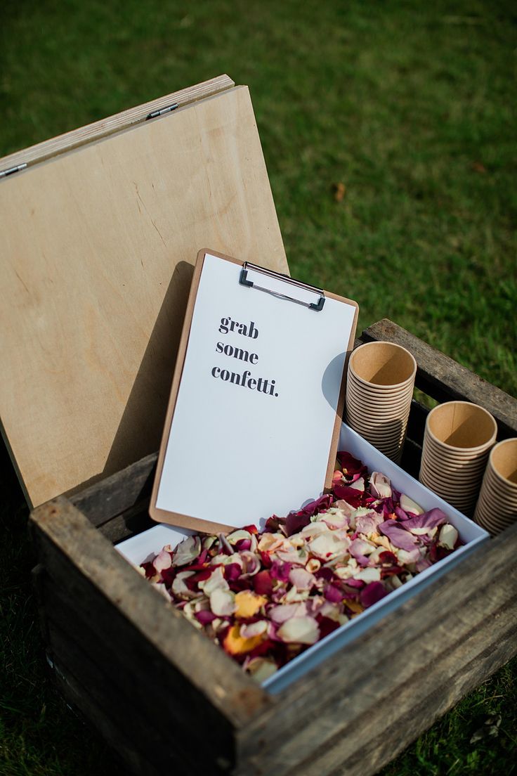 an open wooden box filled with lots of flowers next to paper cups and a sign