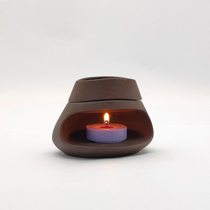 a lit candle in a clay pot on a white surface