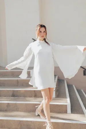 a woman is standing on some steps wearing a white dress and cape over her shoulders