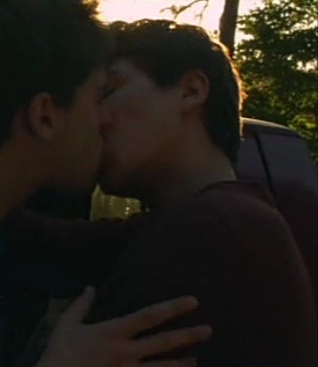 two young men kissing each other in front of a car with the sun behind them