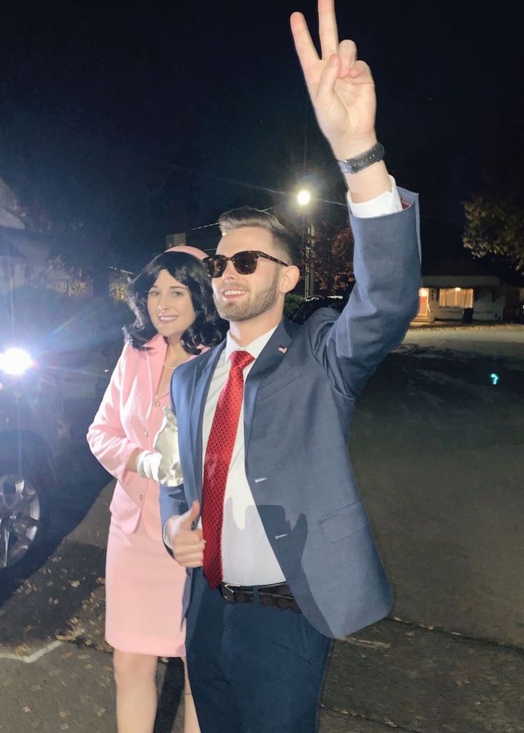 a man in a suit and tie is giving the peace sign with his hand while standing next to a woman