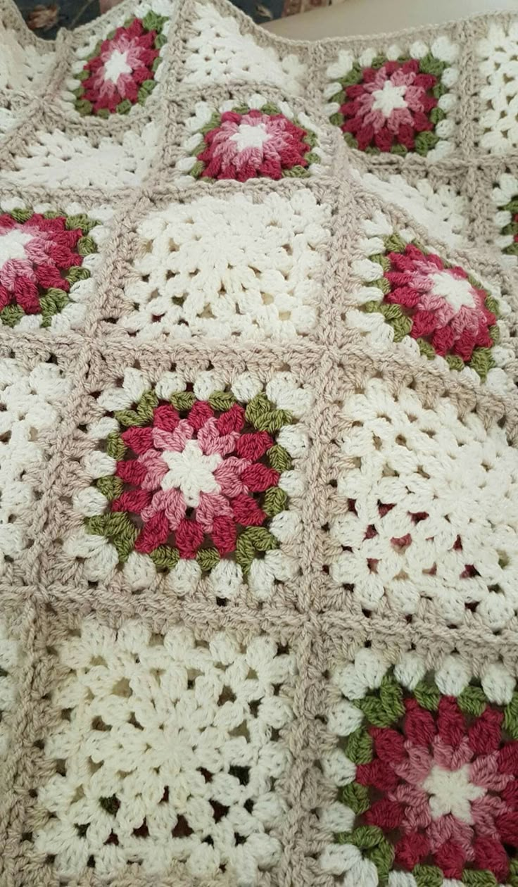 a crocheted blanket with red and white flowers on it is laying on a bed