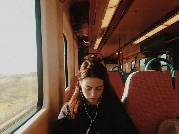 a woman sitting on a train looking at her cell phone and listening to headphones