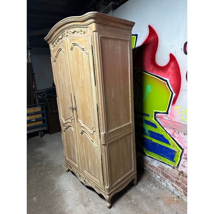 a tall wooden armoire next to a wall with graffiti on it