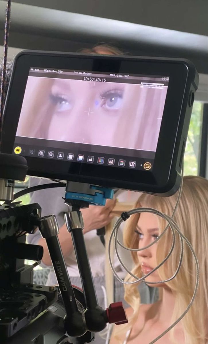 a woman with long blonde hair is looking at an image on the screen while another person stands behind her