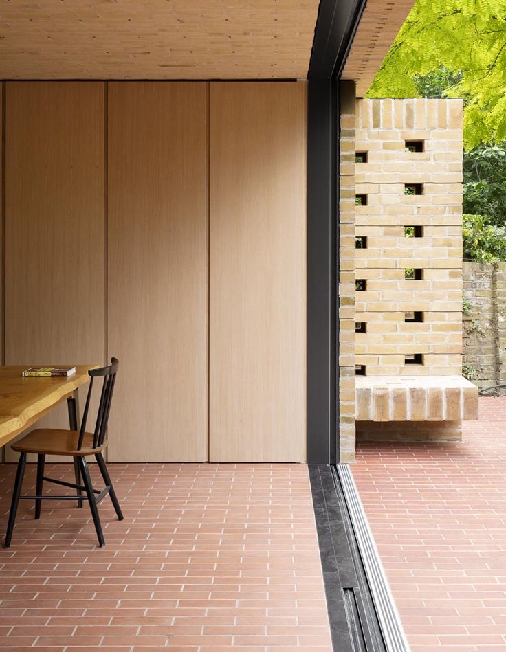 a wooden table sitting next to a window on top of a brick floor covered patio