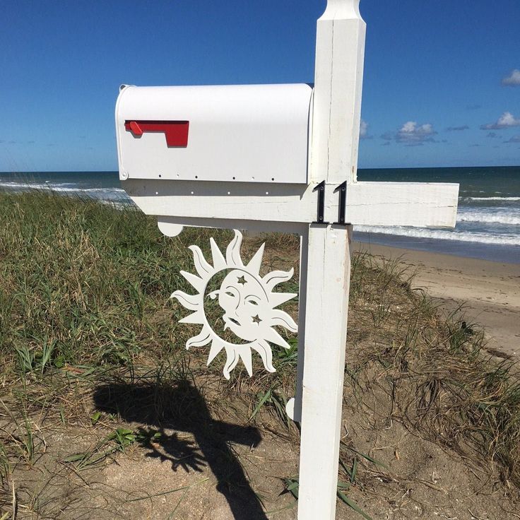 a white mailbox sitting on the side of a sandy beach next to the ocean