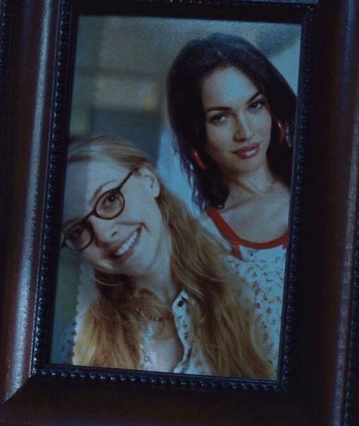 two women with glasses are smiling in front of a framed photo on the wall above them