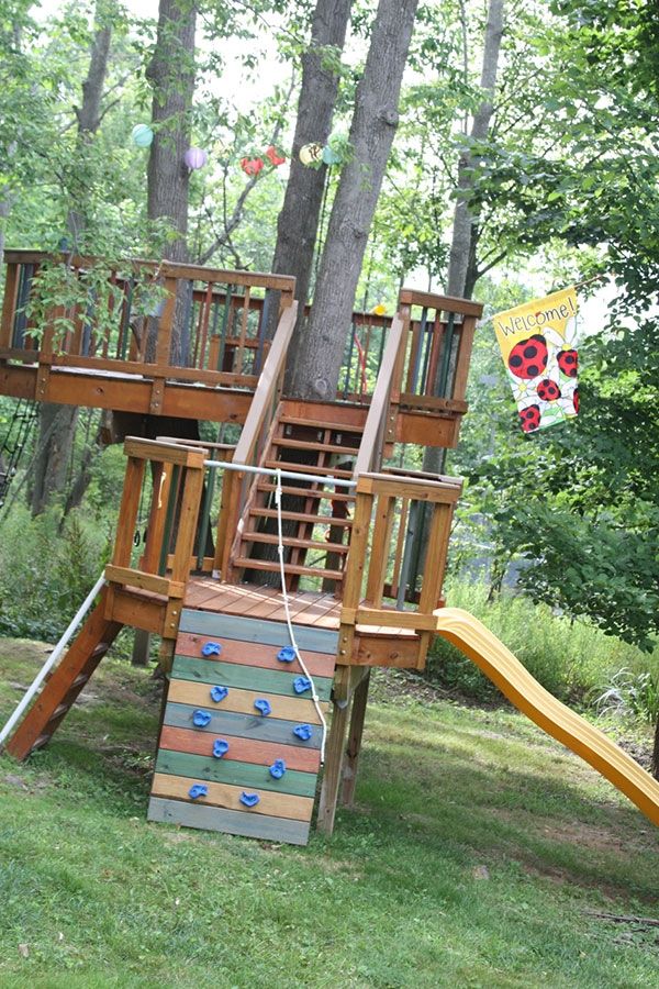 a wooden play set in the middle of a park with a slide and climbing wall