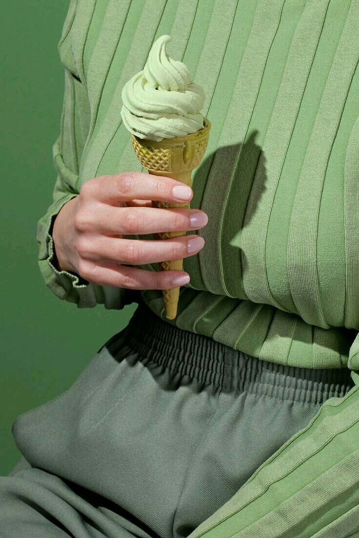 a woman is holding an ice cream cone in her right hand and wearing green pants