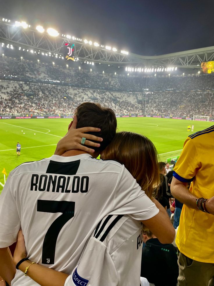 two people hugging each other in front of a crowd at a soccer game with the stadium lights on