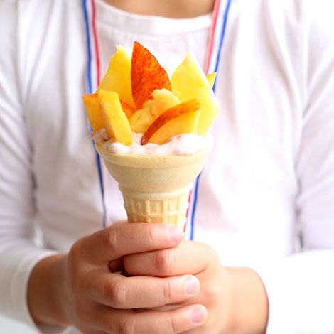 a person holding an ice cream cone with fruit on top