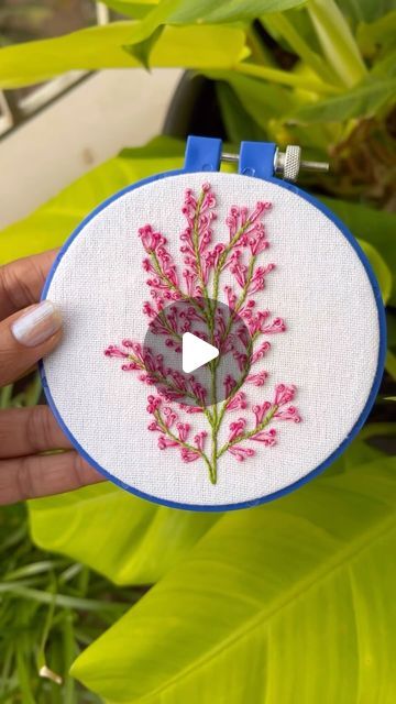 a person holding a small embroidered object with pink flowers on it and a video playing in the background