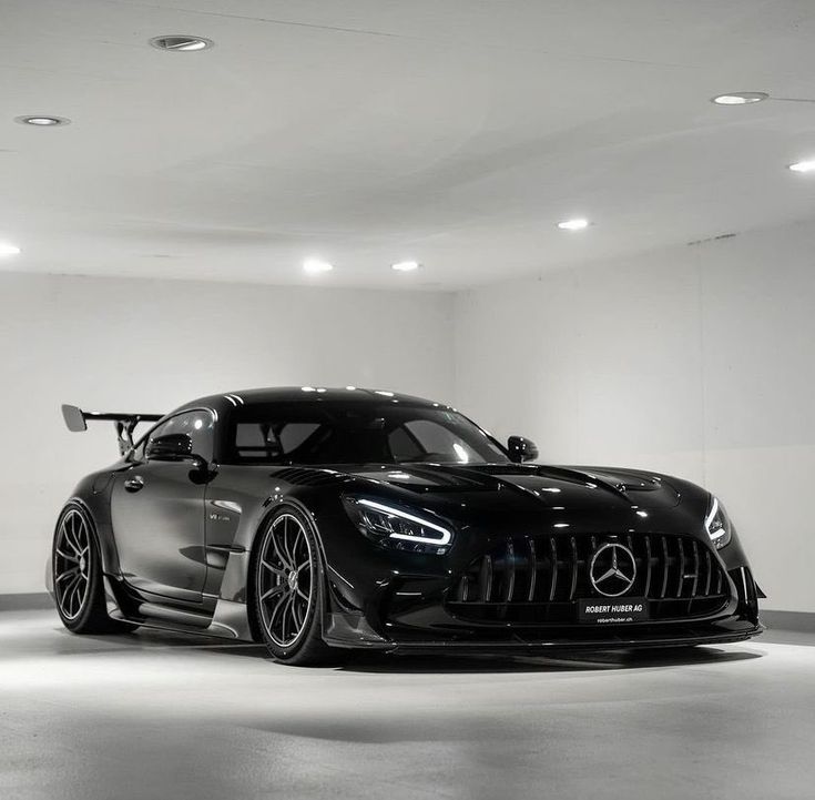 a black mercedes sports car parked in a white room with lights on the ceiling and floor