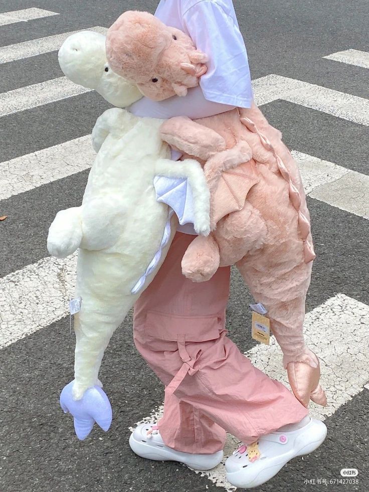 a person holding two stuffed animals in their arms while crossing the street at an intersection