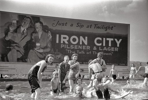 black and white photograph of children playing in the water with an iron city sign behind them