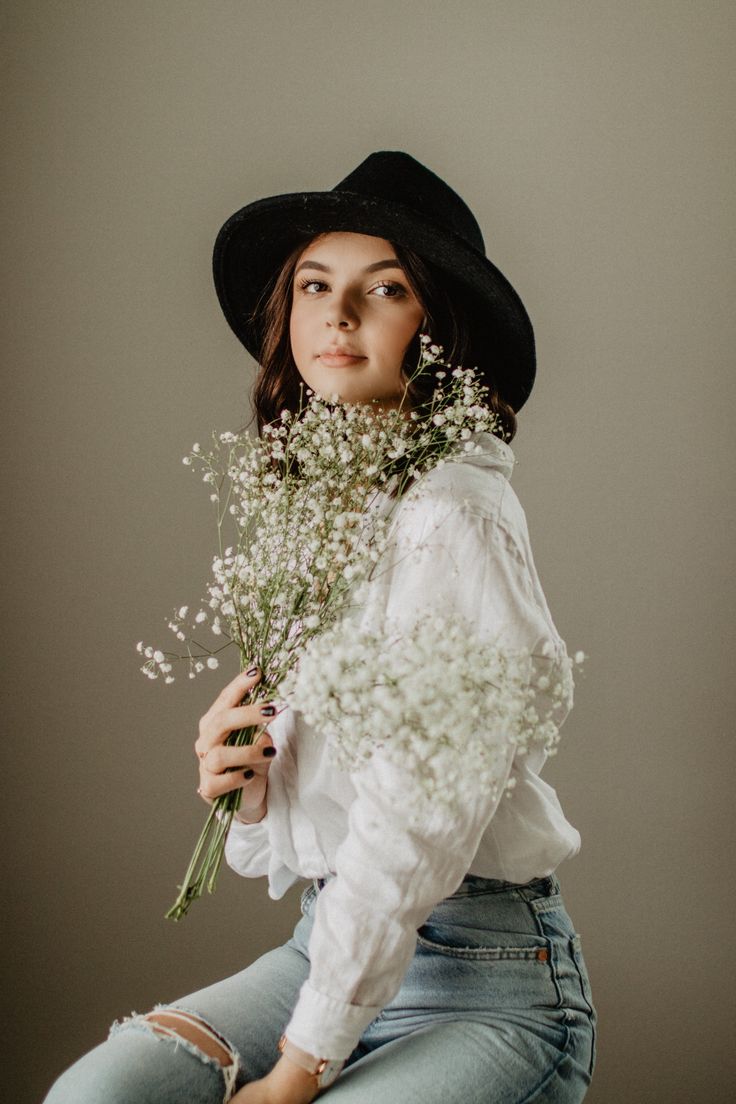 a woman wearing a hat and holding a bunch of flowers in her hands while sitting on the floor