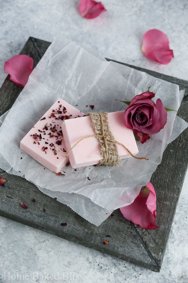 two bars of soap sitting on top of wax paper next to pink flowers and petals