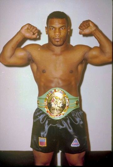 a shirtless man posing for a photo with his arms raised in the air and wearing boxing trunks