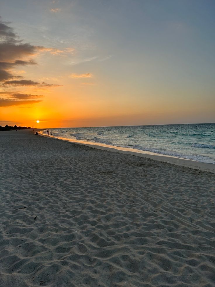 the sun is setting at the beach with people walking on it