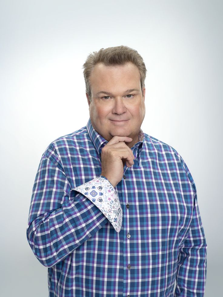 a man in a blue and white checkered shirt posing for the camera with his hand on his chin