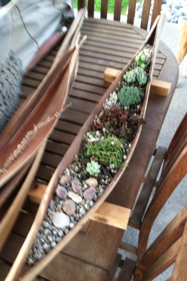 two canoes sitting on top of a table with rocks and plants in them next to each other