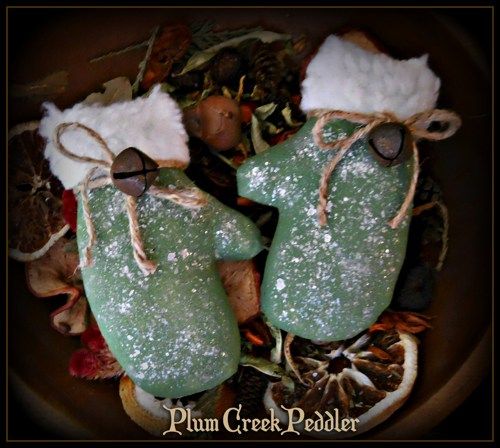 two green mittens sitting on top of a pile of leaves