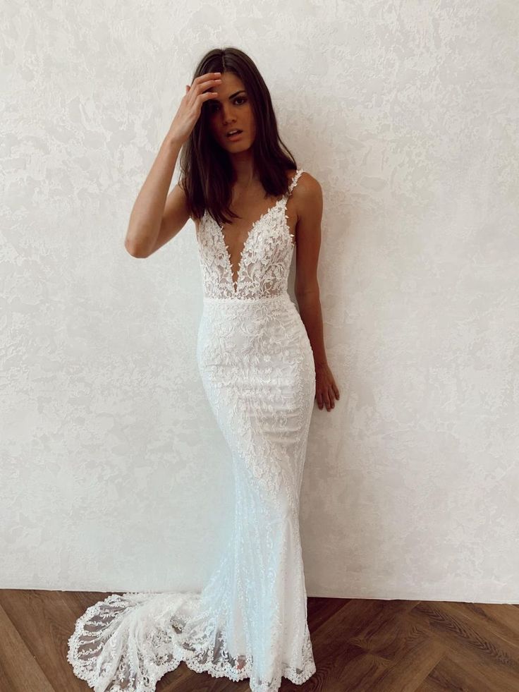 a woman standing in front of a wall wearing a white dress and holding her hand on her head