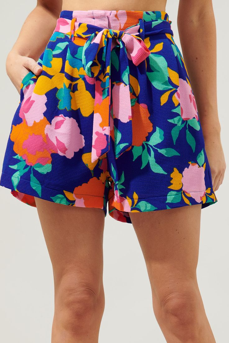 Spend the day basking in the sun, wearing these fitting shorts. Fun colored floral motifs against a blue-ground decorate these breezy shorts that sit high on the hips. A belt is added for a refined feminine look, while the shorts start to widen. They maintain a relaxed fit throughout the hips and thighs.- Hook and clasp- Zipper fly- Pockets- Bubble crepe- Color: Cobalt Pink OrangeSize + Fit - Model is 5'8" and wearing size XS- Measurements taken from size S - Waist: 13"- Inseam: 3" Fabric Self:9 Multicolor Beachwear Shorts For Summer Outings, Blue Tropical Print Beachwear Shorts, Blue Tropical Shorts For Summer, Multicolor Shorts For Summer Outings, Floral Print Shorts For Spring Day Out, Floral Print Beachwear Bottoms For Spring, Blue Summer Shorts With Elastic Waistband, Blue Tropical Print Shorts, Spring Beachwear Shorts For Day Out