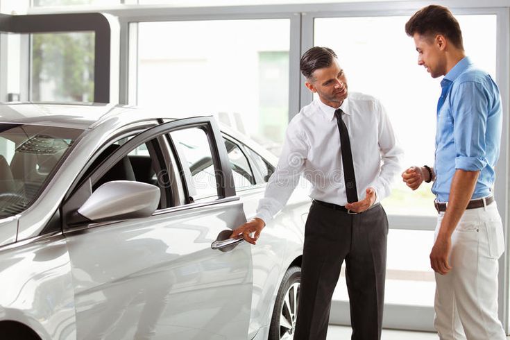 two men standing next to each other in front of a white car with the door open