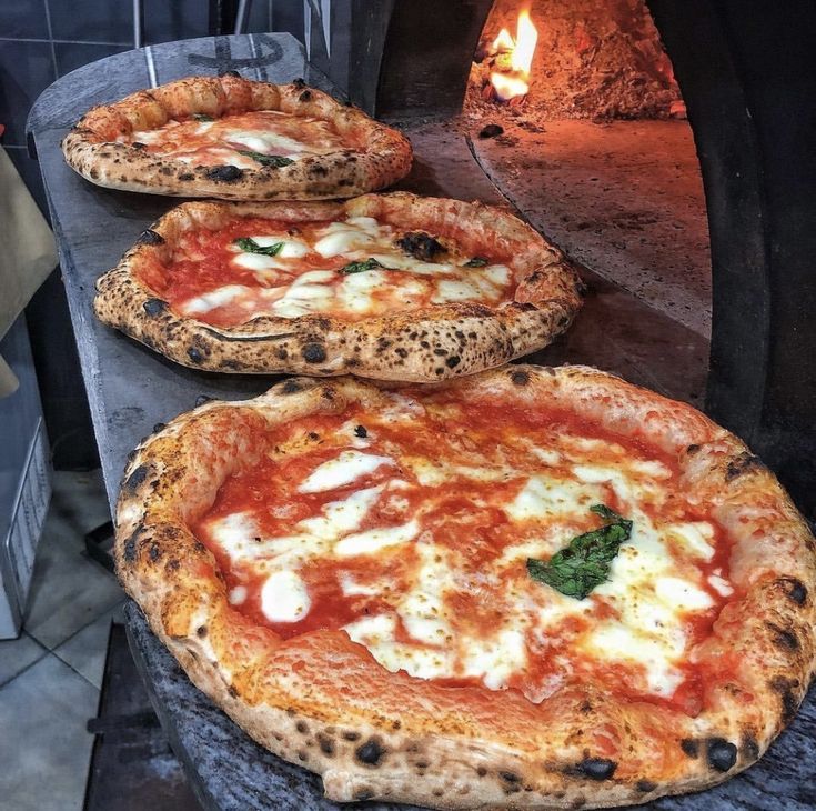 three pizzas sitting on top of a stone counter next to an open fire oven