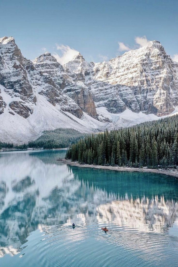 the mountains are covered in snow and there is a body of water with two canoes on it